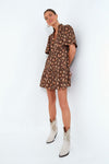 A woman wears a Tuckernuck flutter sleeve mini dress in rosewood chintz print with white cowboy boots.