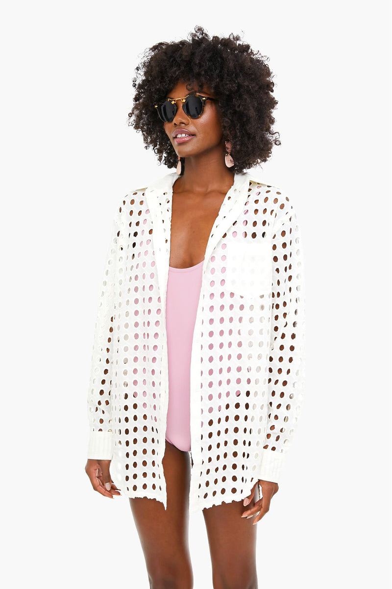 A woman stands confidently in Solid & Striped sunglasses, a light pink swimsuit, and a white mesh beach coverup featuring large circular cutouts.