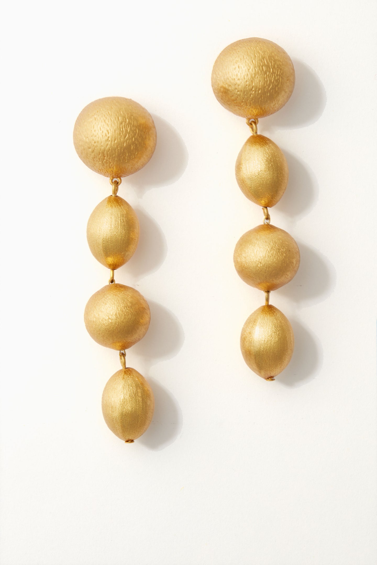 A pair of gold drop earrings by Tuckernuck Jewelry featuring a textured round stud and three oval beads hanging vertically—perfect statement jewelry.