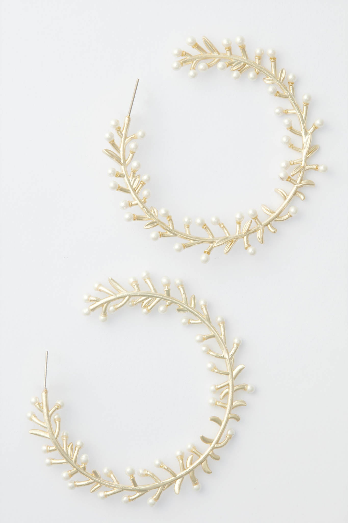 Nicola Bathie's large, circular gold hoop earrings are adorned with delicate pearls and leaf-shaped accents, creating a floral bud-inspired design.