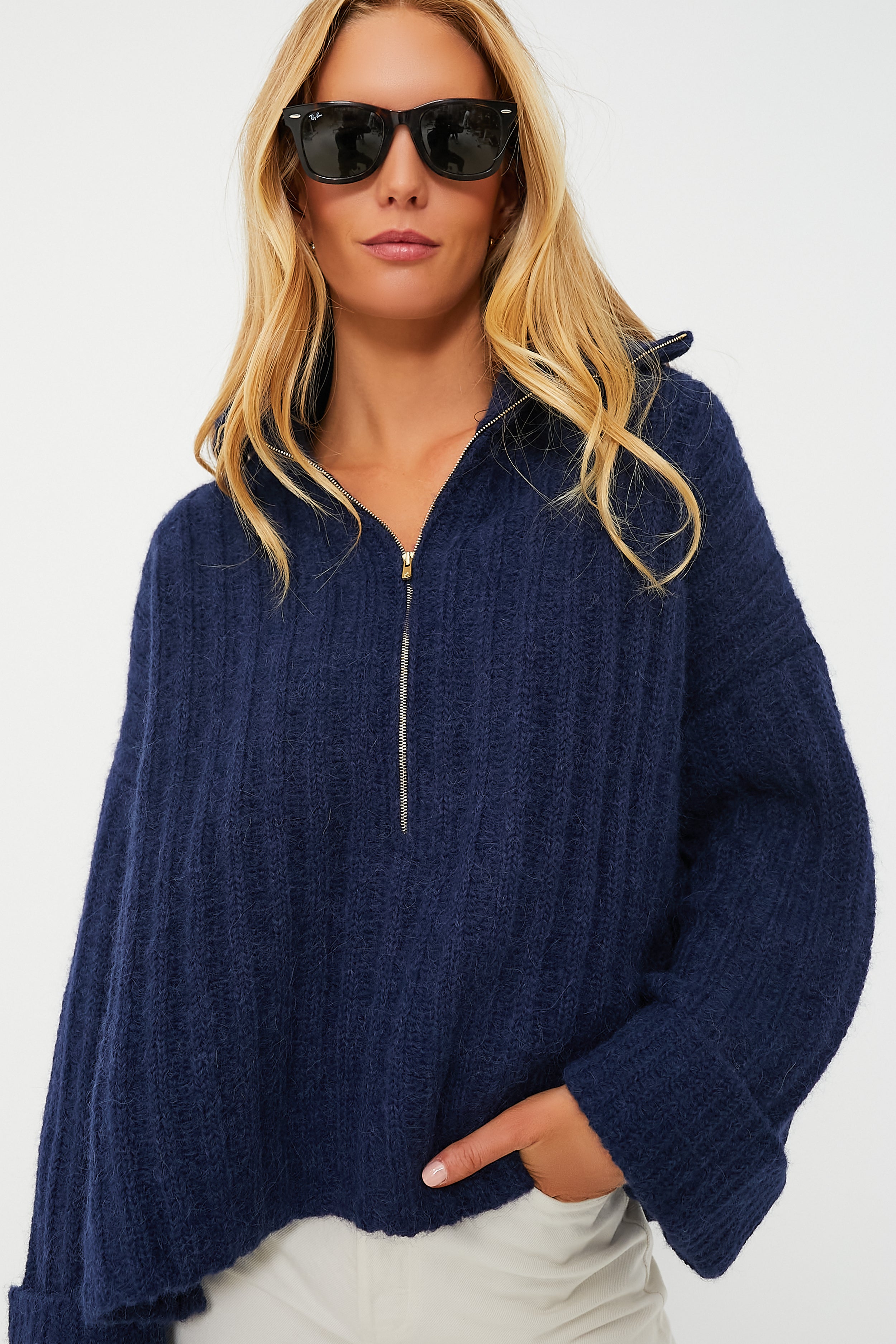 A woman models ELEVEN SIX's navy blue oversized sweater with Andean-inspired knitwork, paired with black sunglasses and light-colored pants, her hand in the pocket.