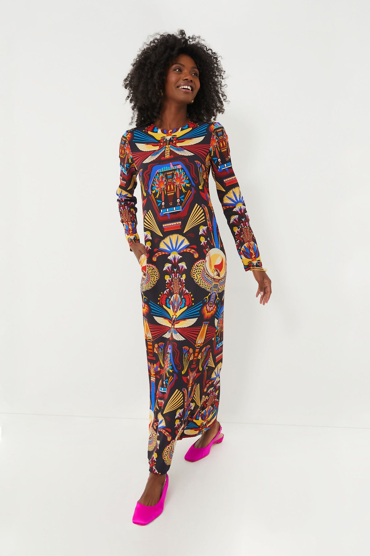 A woman smiles and looks to the side while wearing the La DoubleJ Nephthys Dress, a maxi dress featuring a vibrant multicolor print with geometric and abstract patterns.