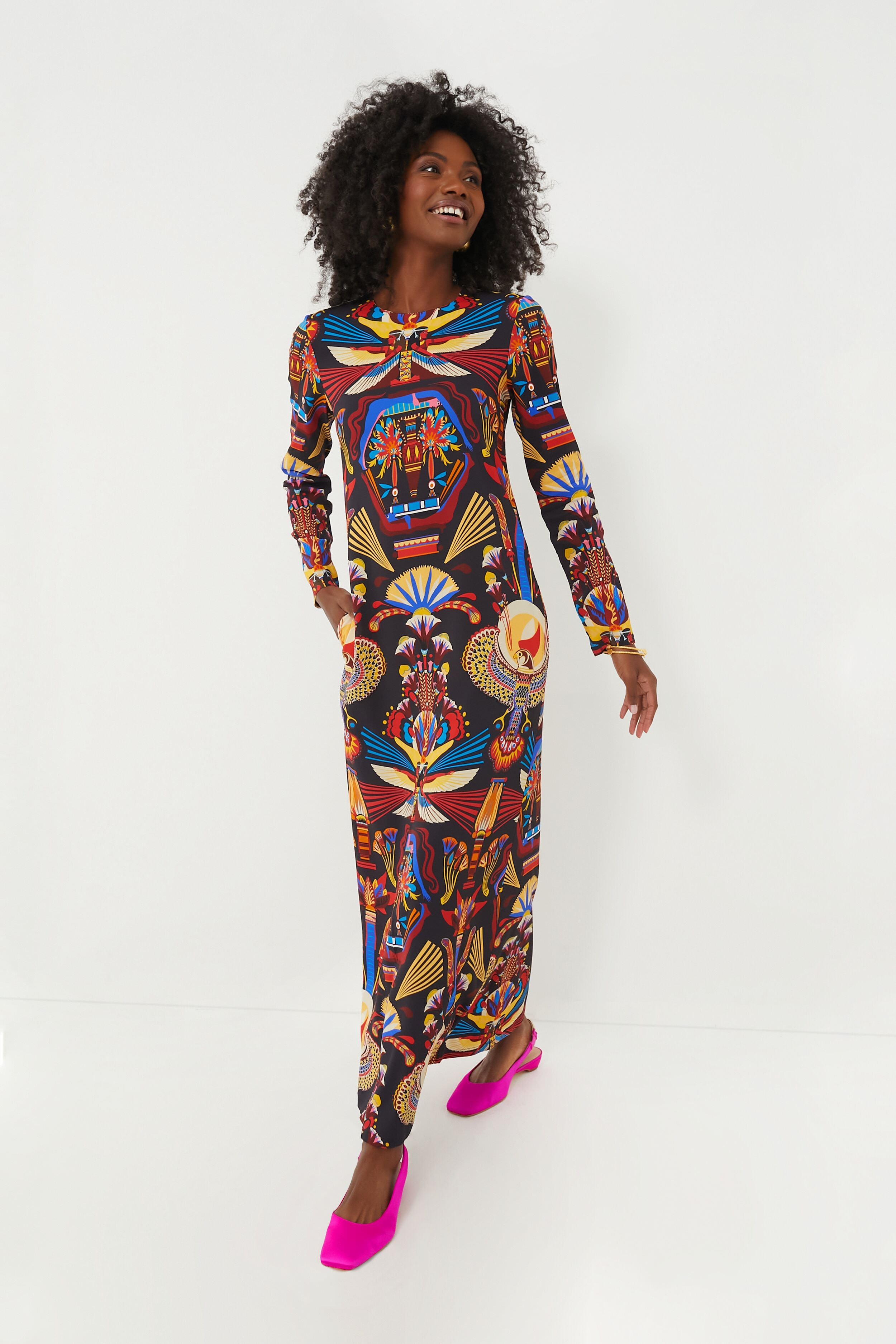 A woman smiles and looks to the side while wearing the La DoubleJ Nephthys Dress, a maxi dress featuring a vibrant multicolor print with geometric and abstract patterns.