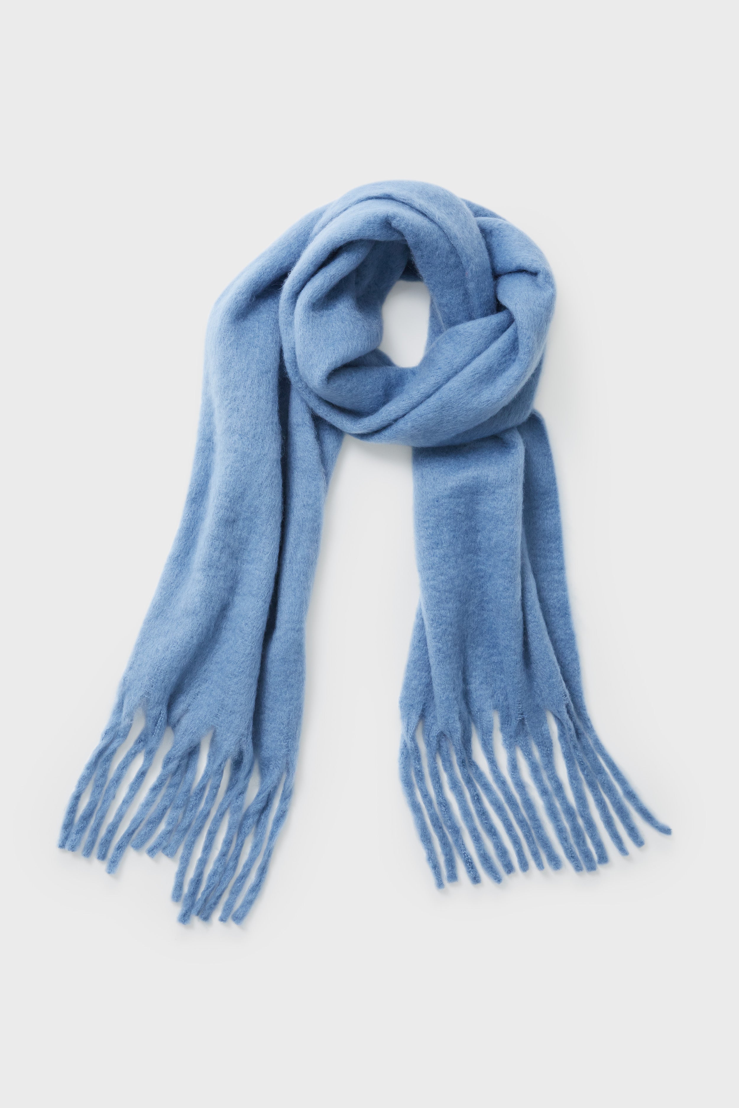 A light blue Hat Attack wool Denim Chic Solid Scarf with fringed ends, stylishly laid out as a cozy cold-weather accessory.