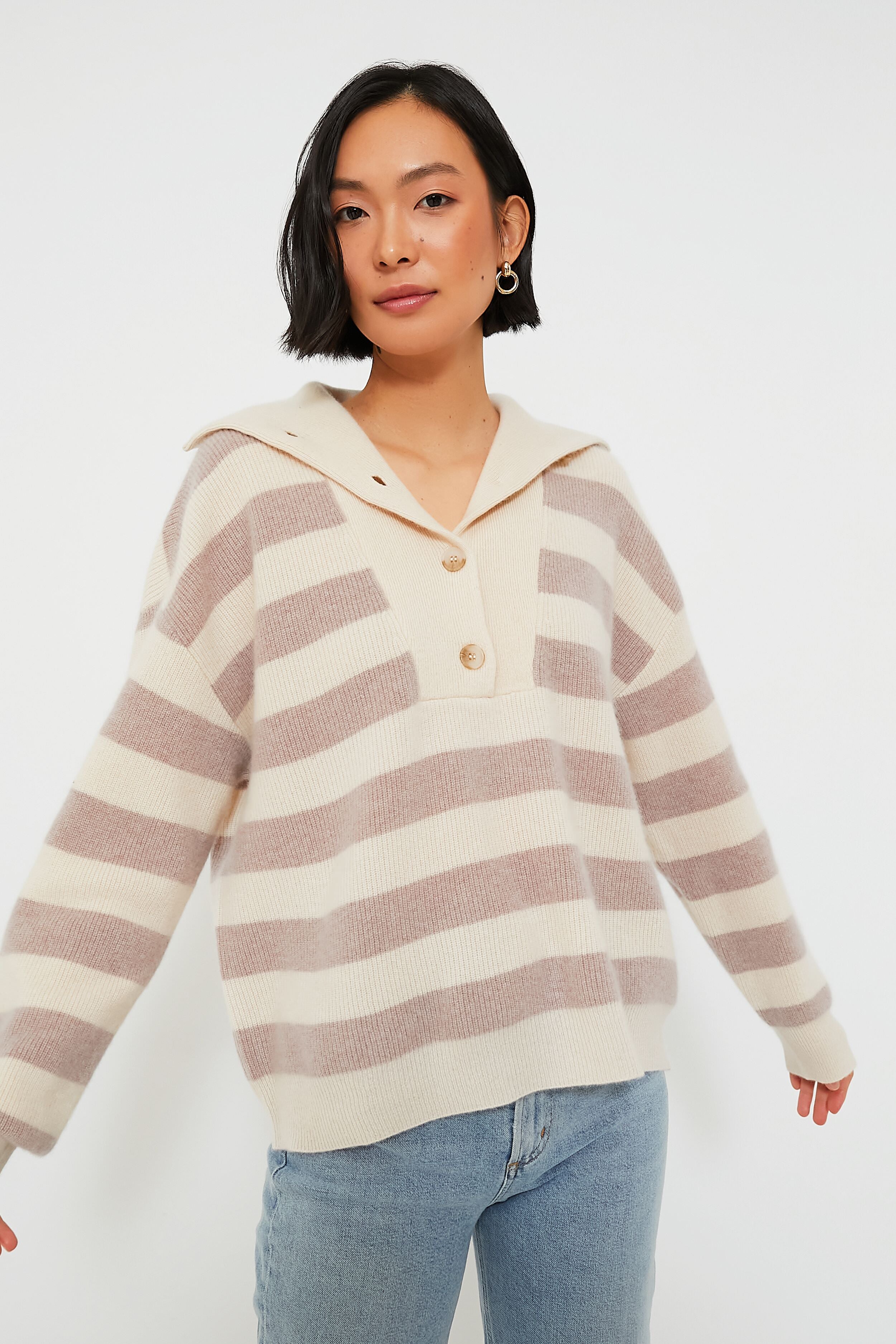 A person wears a cream and beige striped XiRENA pullover sweater with a collar and buttons, paired with light blue jeans.