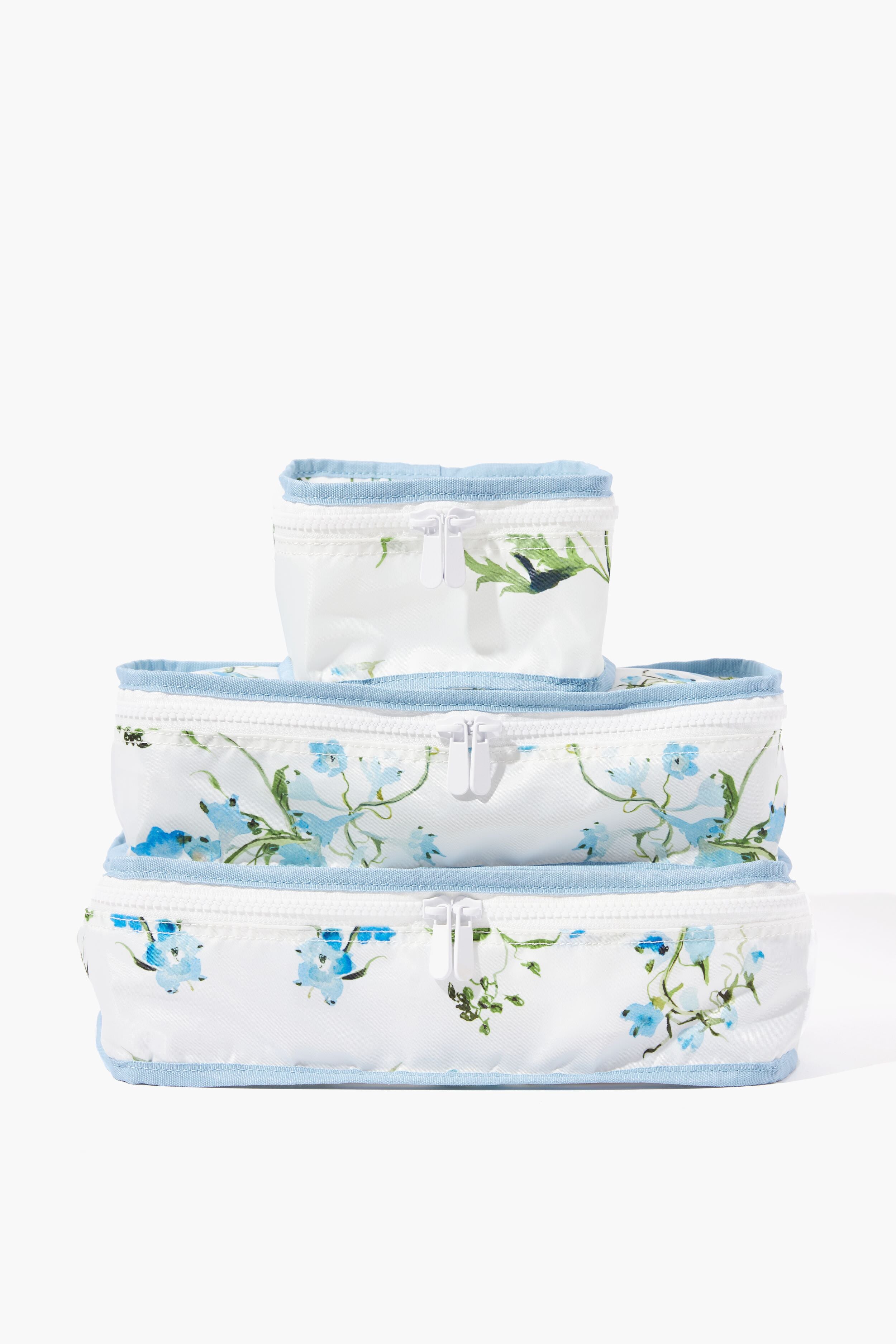 The Neely & Chloe x Inslee set features three white nylon zipper pouches with blue floral designs and light blue trim, stacked by size—ideal for travel organization.
