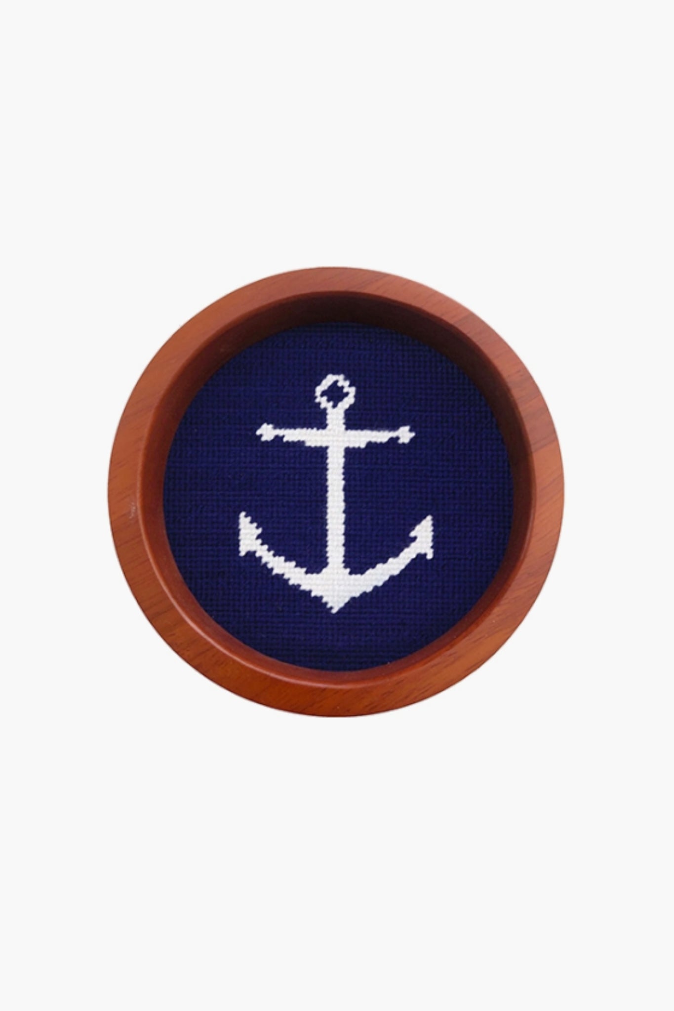 A round wooden frame by Smathers and Branson showcases a hand-stitched white anchor needlepoint on dark blue fabric.