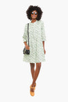 A person wears a green floral Tuckernuck Royal Shirt Dress with silky smooth fabric, sunglasses, brown shoes, and a black crossbody bag—a true closet staple.
