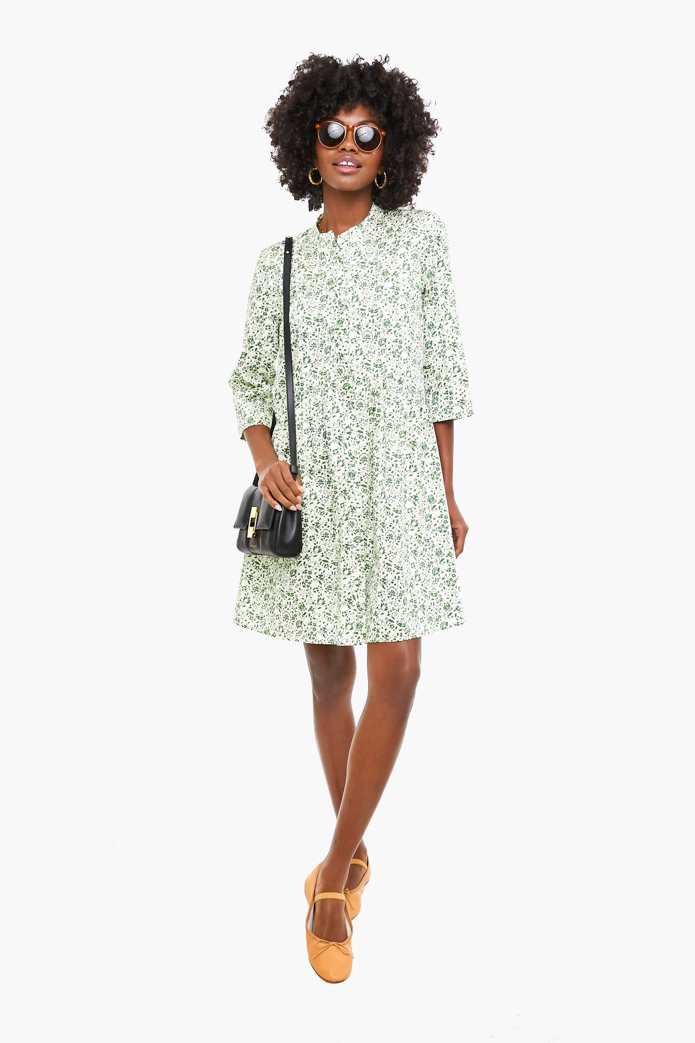 A person wears a green floral Tuckernuck Royal Shirt Dress with silky smooth fabric, sunglasses, brown shoes, and a black crossbody bag—a true closet staple.