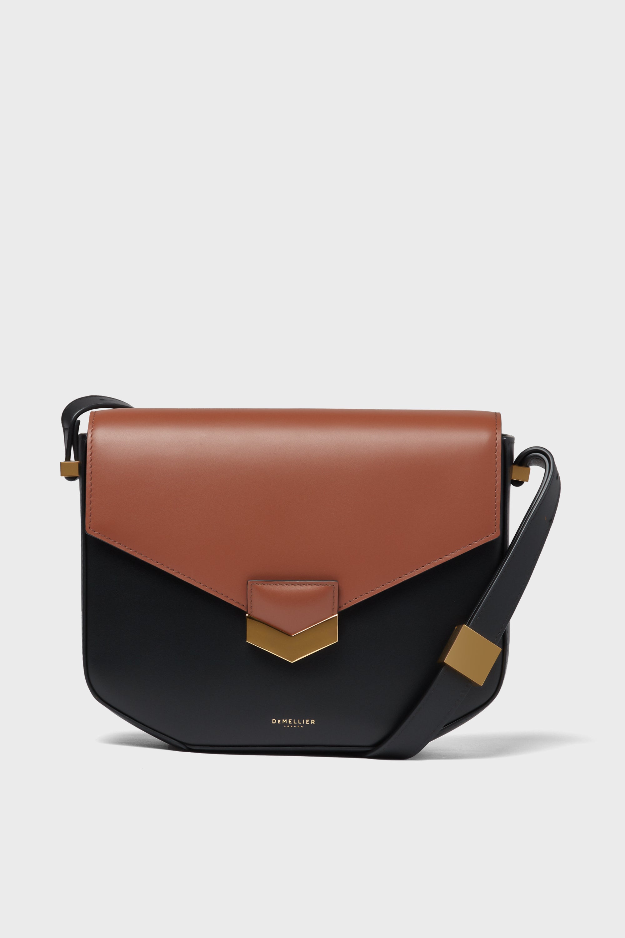 The Demellier crossbody bag features a two-tone design with a brown flap, black body, gold-tone hardware, and an adjustable strap.