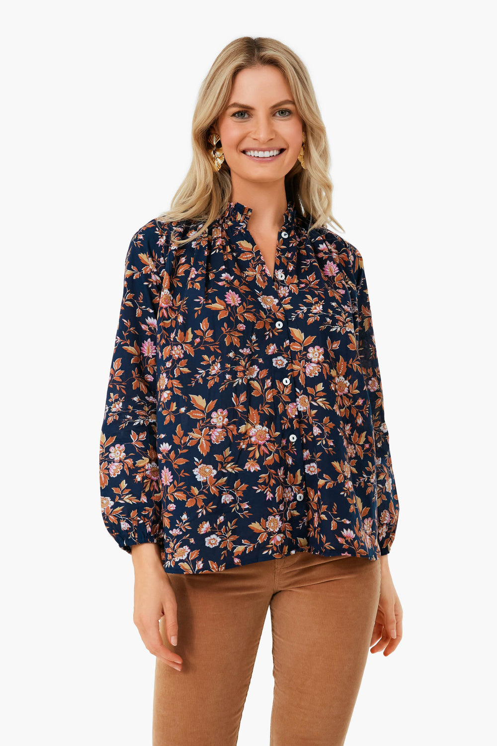 Woman standing and smiling, wearing the Mille Montmarte Francesca Top—a navy 100% cotton blouse with a pink and brown floral print, ruffle collar—paired with tan pants.