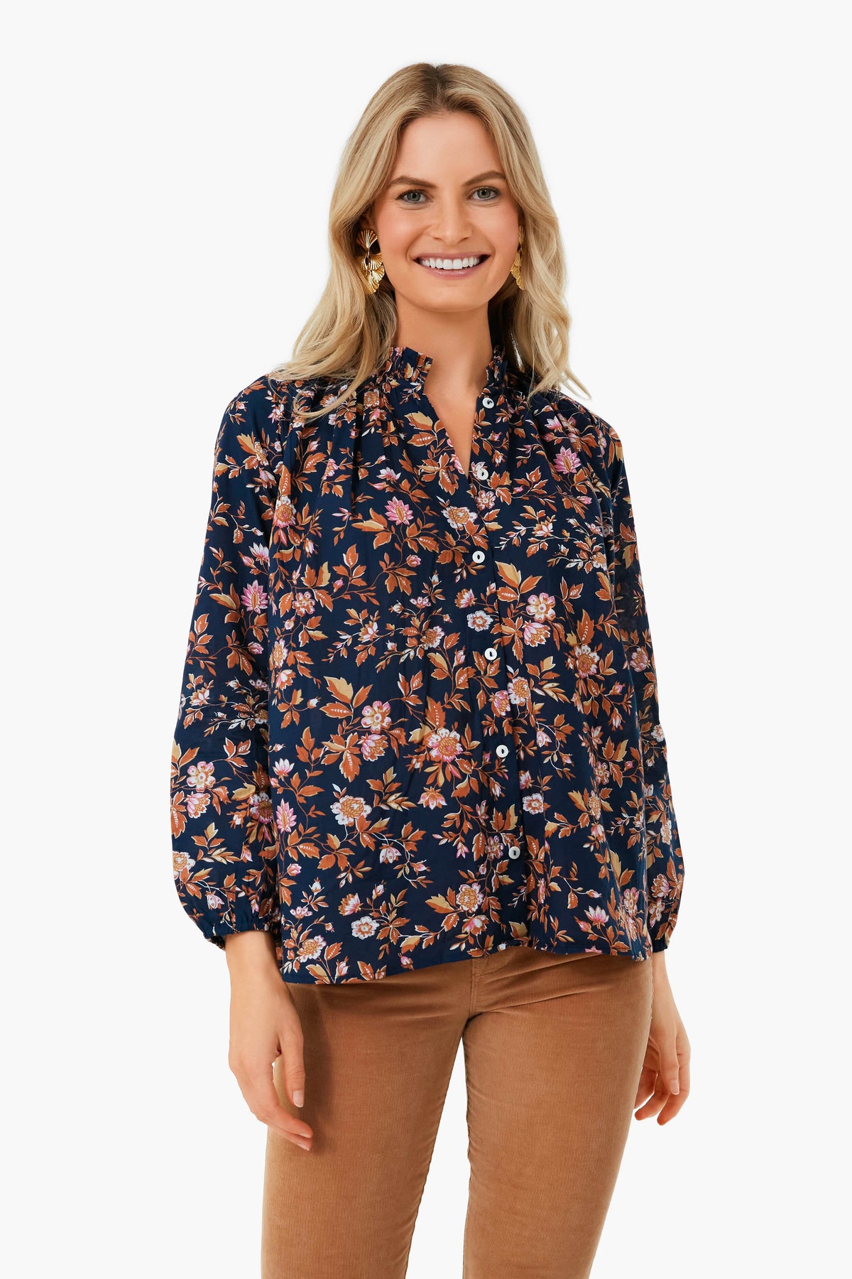 Woman standing and smiling, wearing the Mille Montmarte Francesca Top—a navy 100% cotton blouse with a pink and brown floral print, ruffle collar—paired with tan pants.