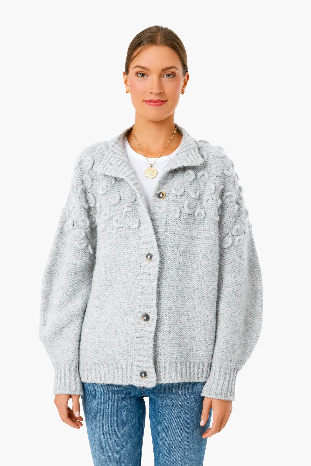 A woman stands facing forward wearing a MIRTH light gray alpaca cardigan with textured detailing, a white shirt, and blue jeans.