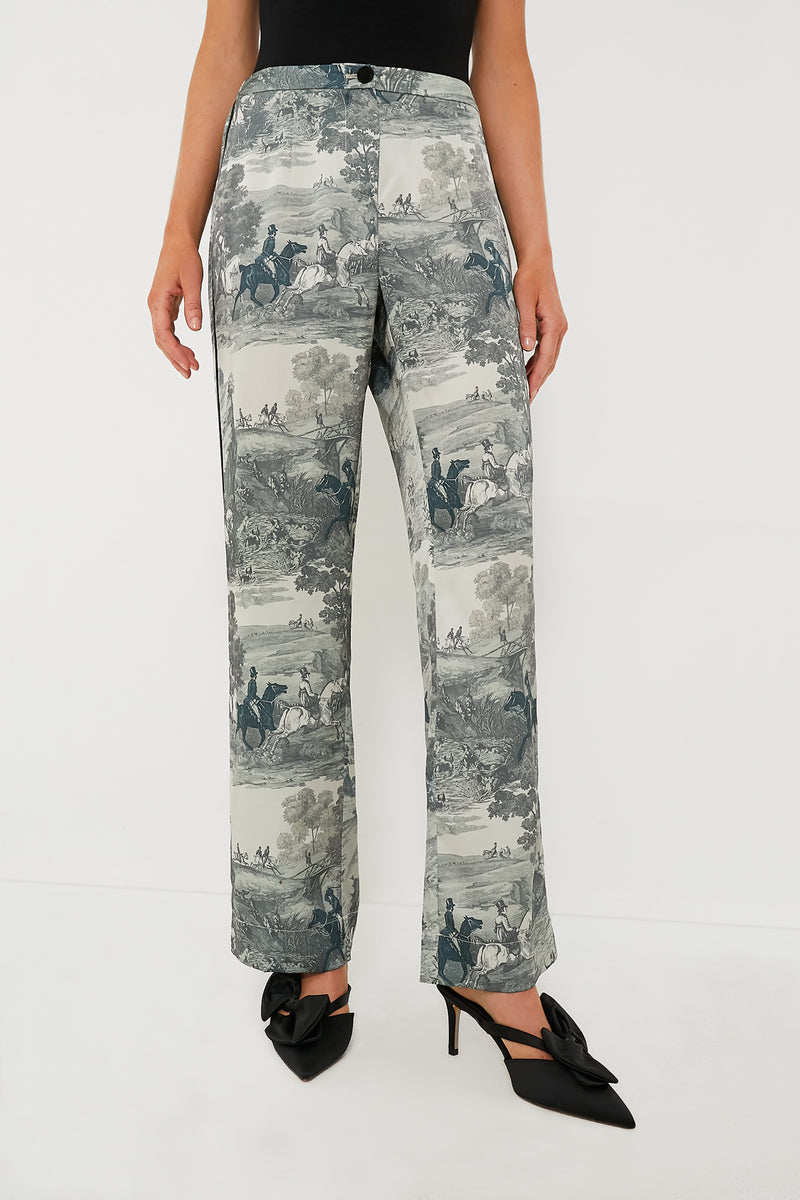 A person styled in high-rise Tuckernuck Middleburg Toile Solene Pants with a scenic print, paired with a black top and black heeled bow shoes.