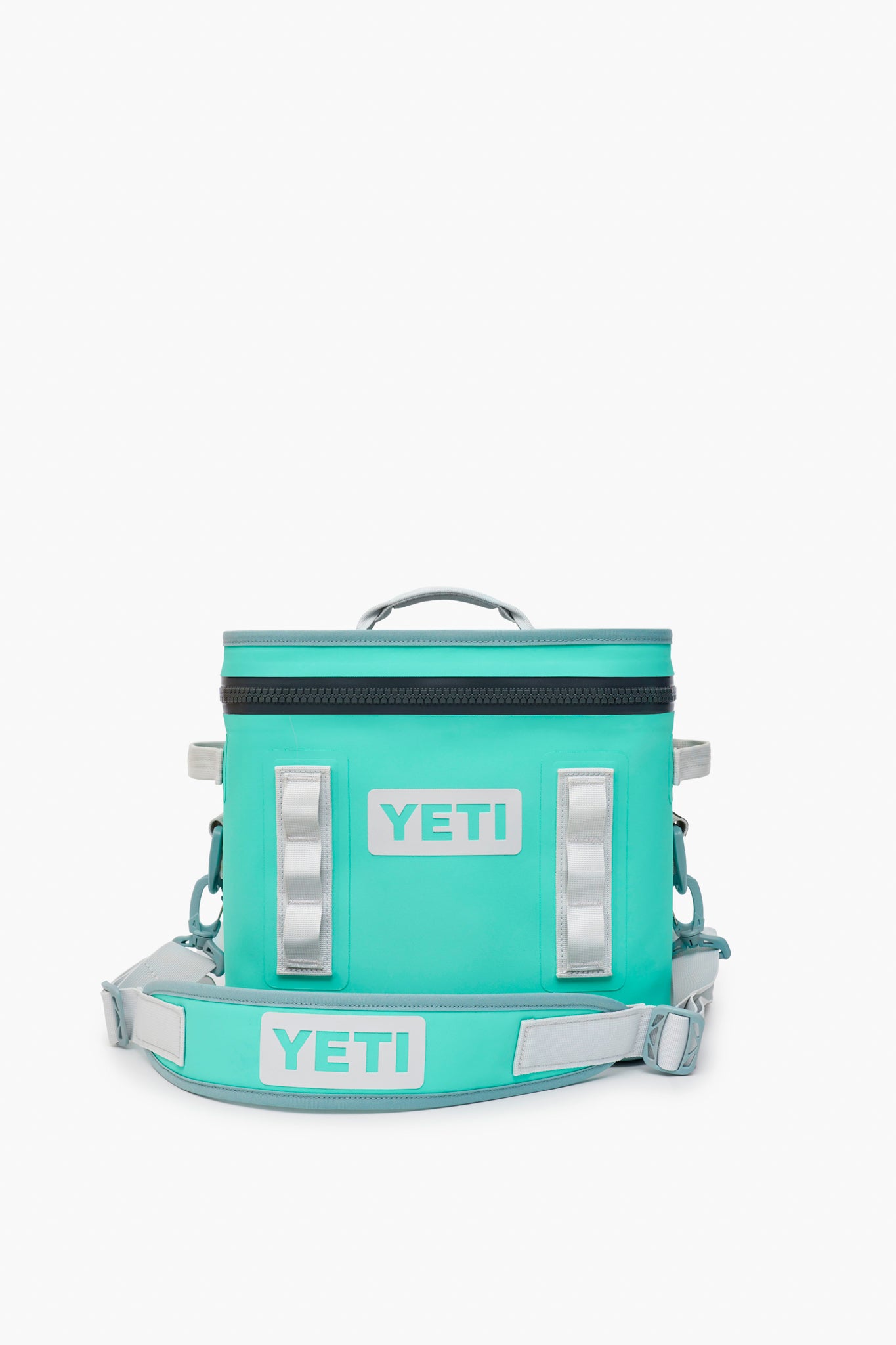 The YETI Hopper Flip Soft Cooler in turquoise features a zipper top, handle, adjustable shoulder strap with YETI branding, and offers durable, waterproof insulation to keep drinks cold.