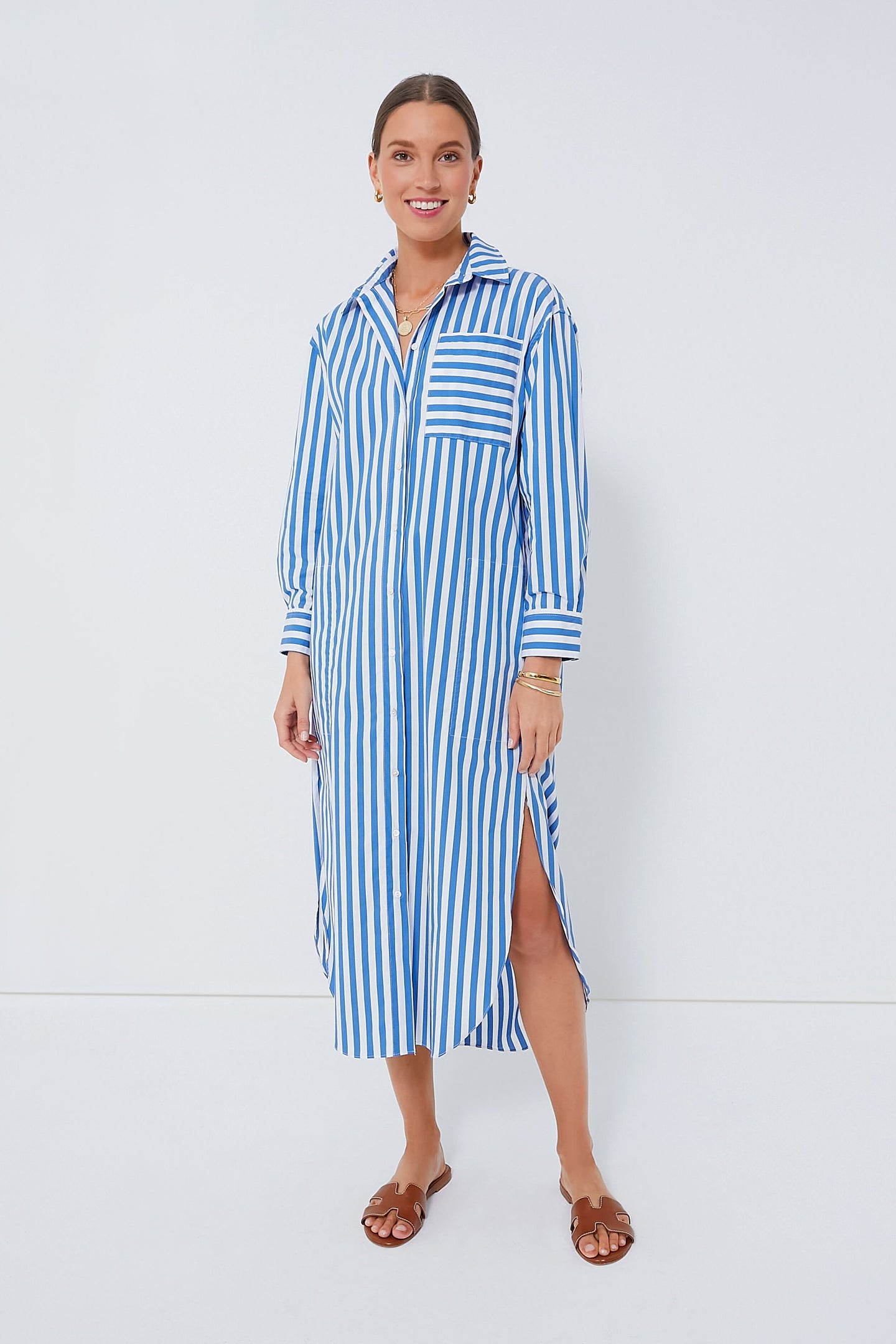 A woman wears a Pomander Place blue and white striped shirt dress with a side slit, brown sandals, and a stylish maxi length.