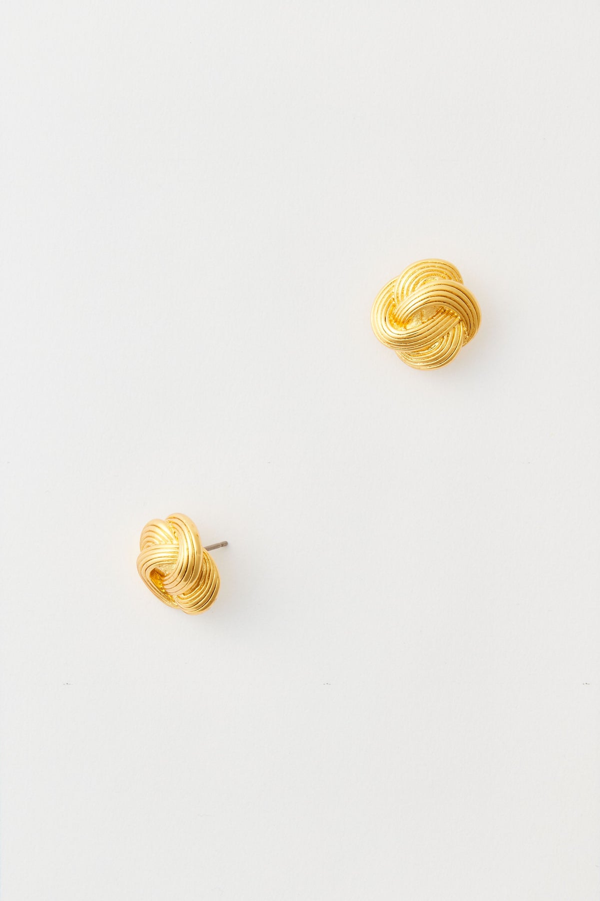 The image shows a pair of Tuckernuck Jewelry gold stud earrings with a classic knot design, crafted from nickel-free materials.