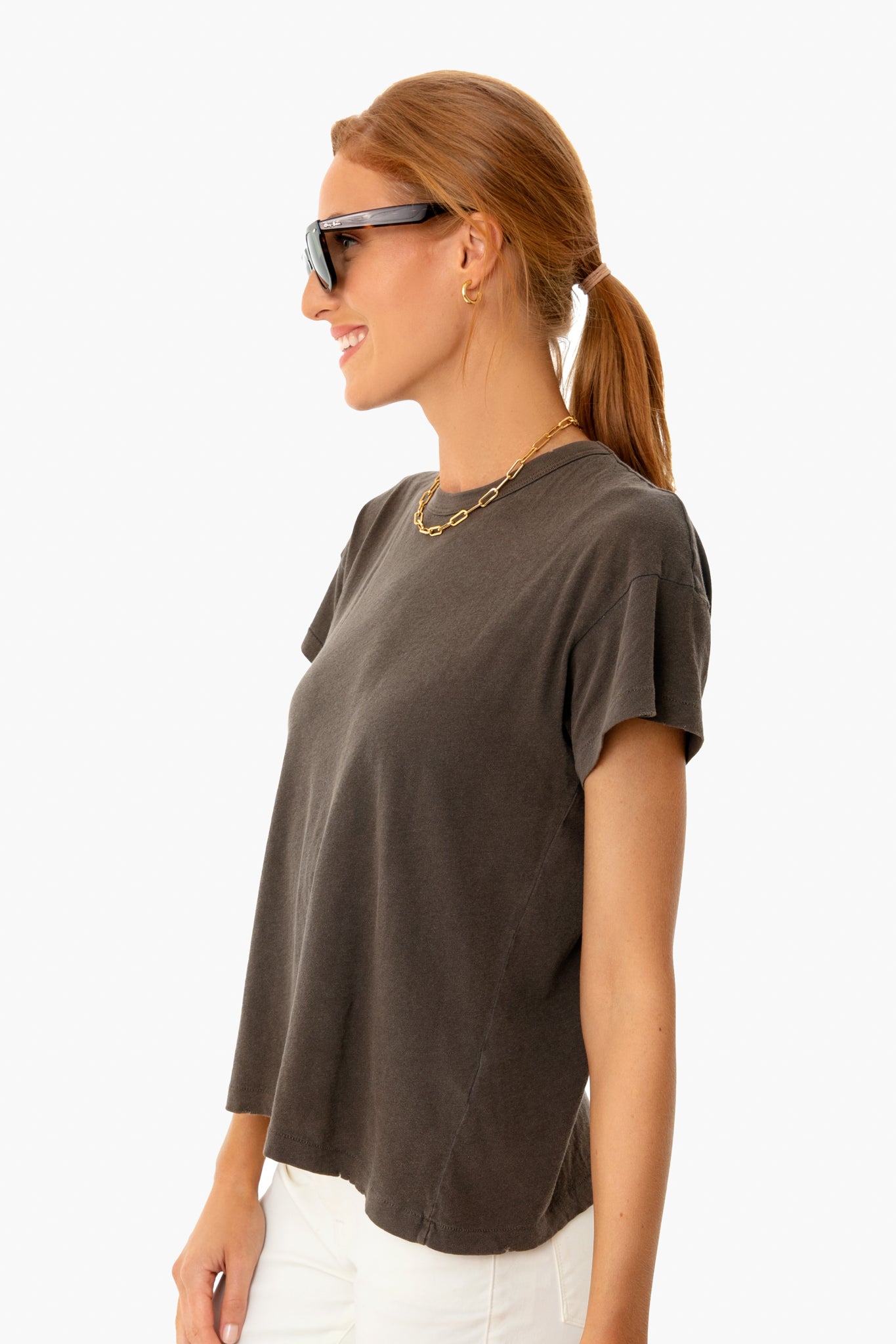 Young woman in oversized sunglasses wearing THE GREAT's Chestnut Boxy Crew Tee; a classic, effortless, high-end staple with a boxy fit and flattering sleeves.
