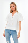 A woman wears a Pomander Place White Tie Front Robbie Top with light blue ripped jeans, posing confidently.