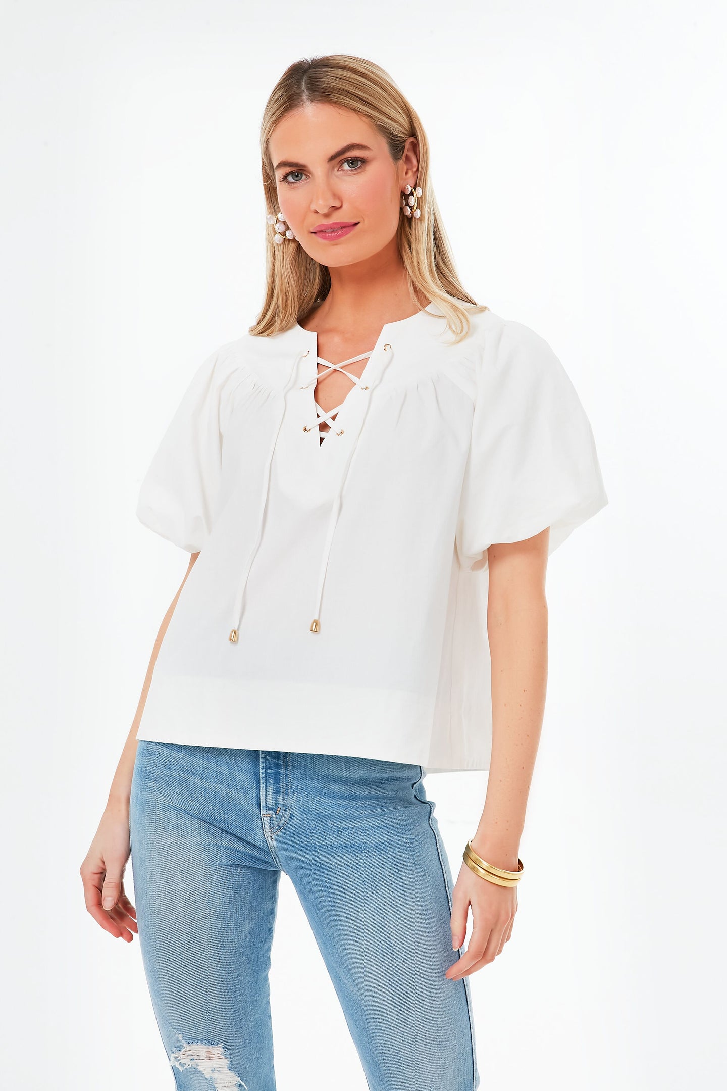 A woman wears a Pomander Place White Tie Front Robbie Top with light blue ripped jeans, posing confidently.