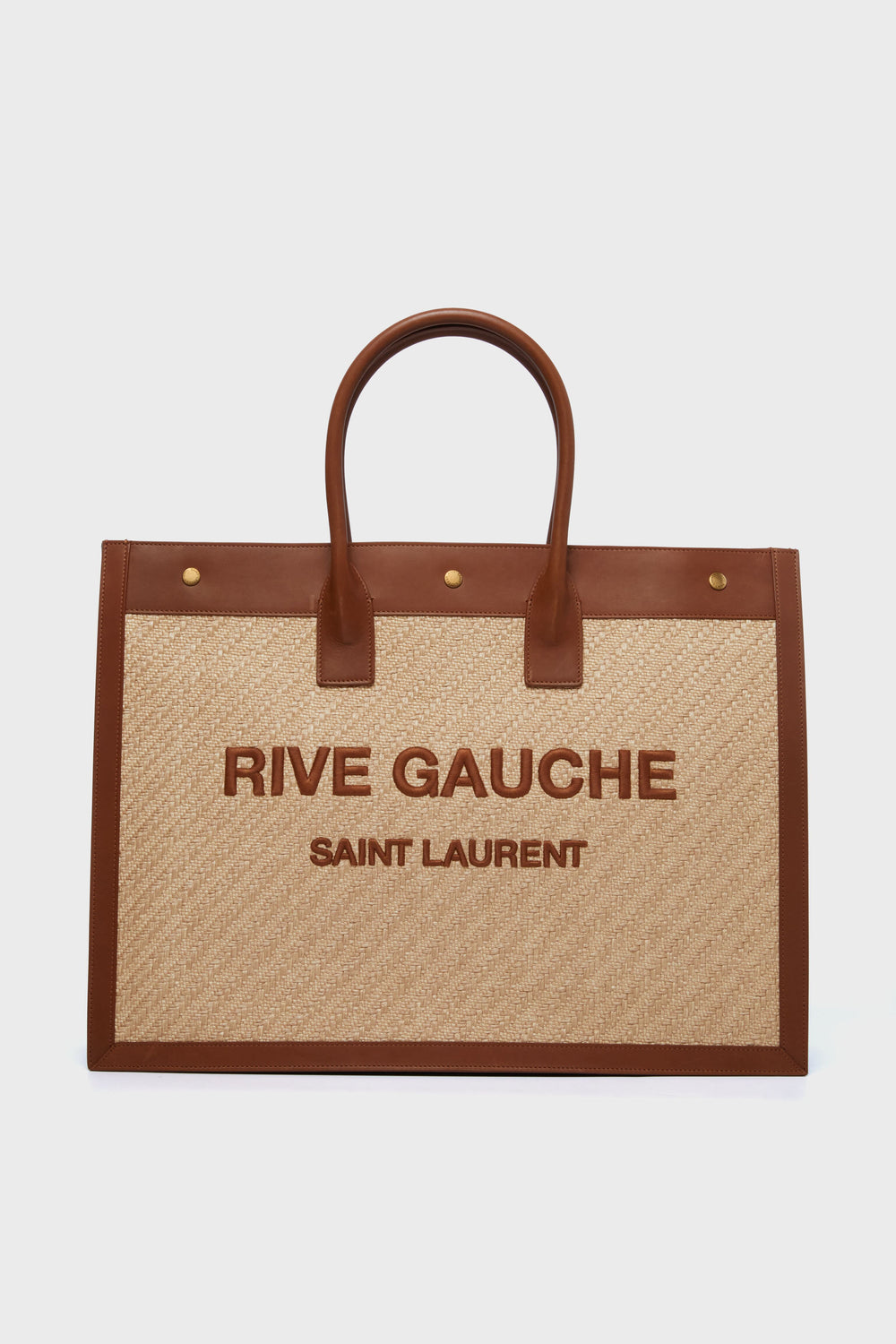 A luxury leather Tuckernuck Archive Collection tote bag with brown handles and trim, featuring RIVE GAUCHE SAINT LAURENT text on a beige woven body.