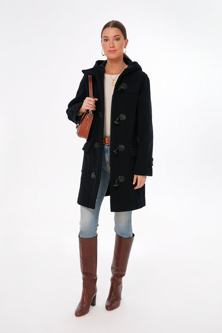 A woman wears a Saint James Navy Venus Coat in a wool blend, light jeans, brown knee-high boots, a beige top, and carries a brown shoulder bag.