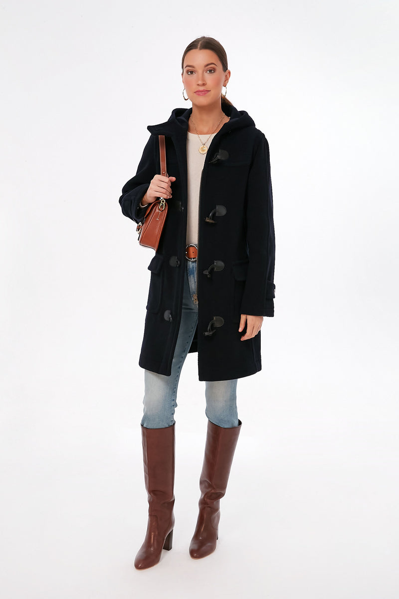 A woman wears a Saint James Navy Venus Coat in a wool blend, light jeans, brown knee-high boots, a beige top, and carries a brown shoulder bag.