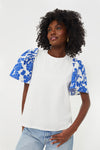 A woman stands confidently in a Hyacinth House Shelby Tee with blue floral puff sleeves and light blue jeans.