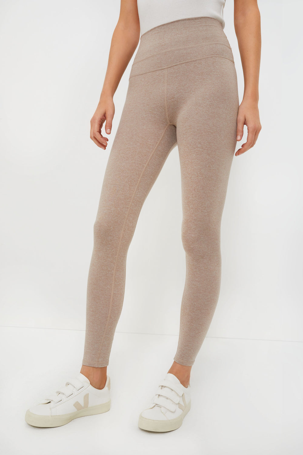 A person wearing high-waisted beige marled jersey leggings from Varley and white sneakers.