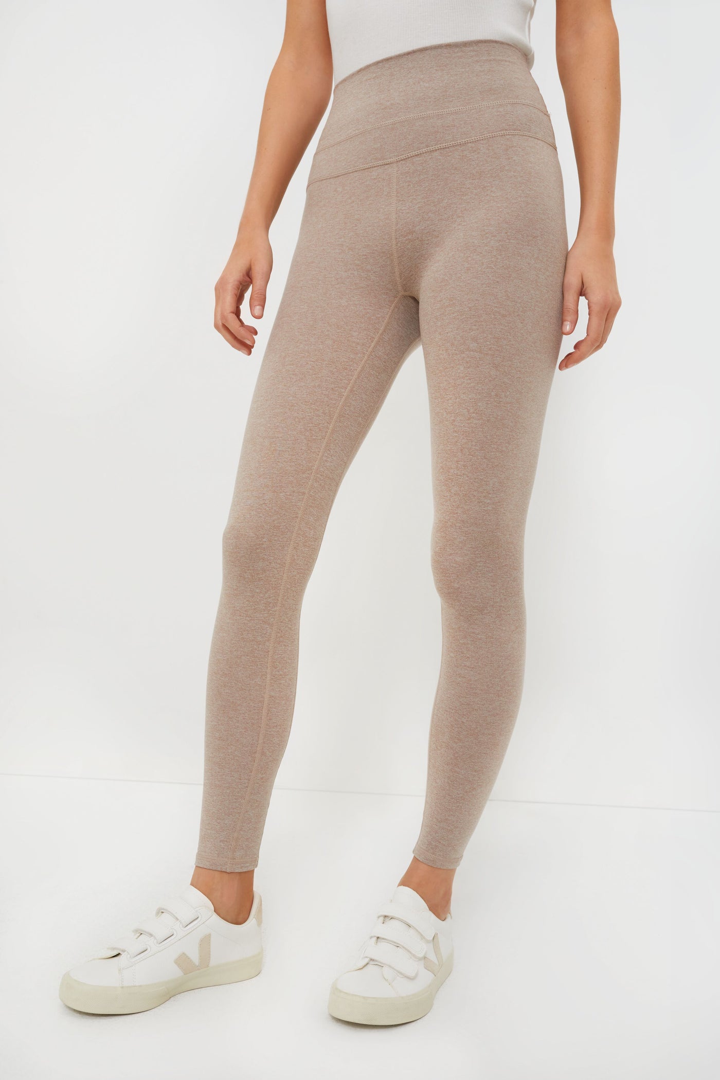 A person wearing high-waisted beige marled jersey leggings from Varley and white sneakers.