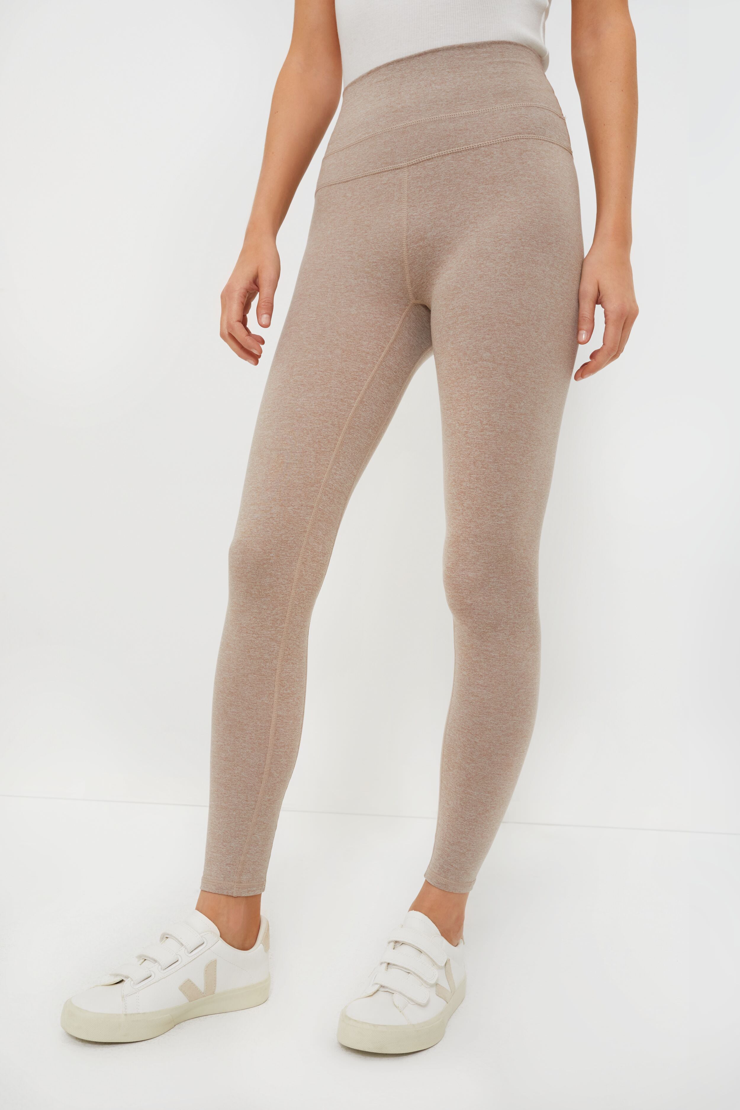 A person wearing high-waisted beige marled jersey leggings from Varley and white sneakers.