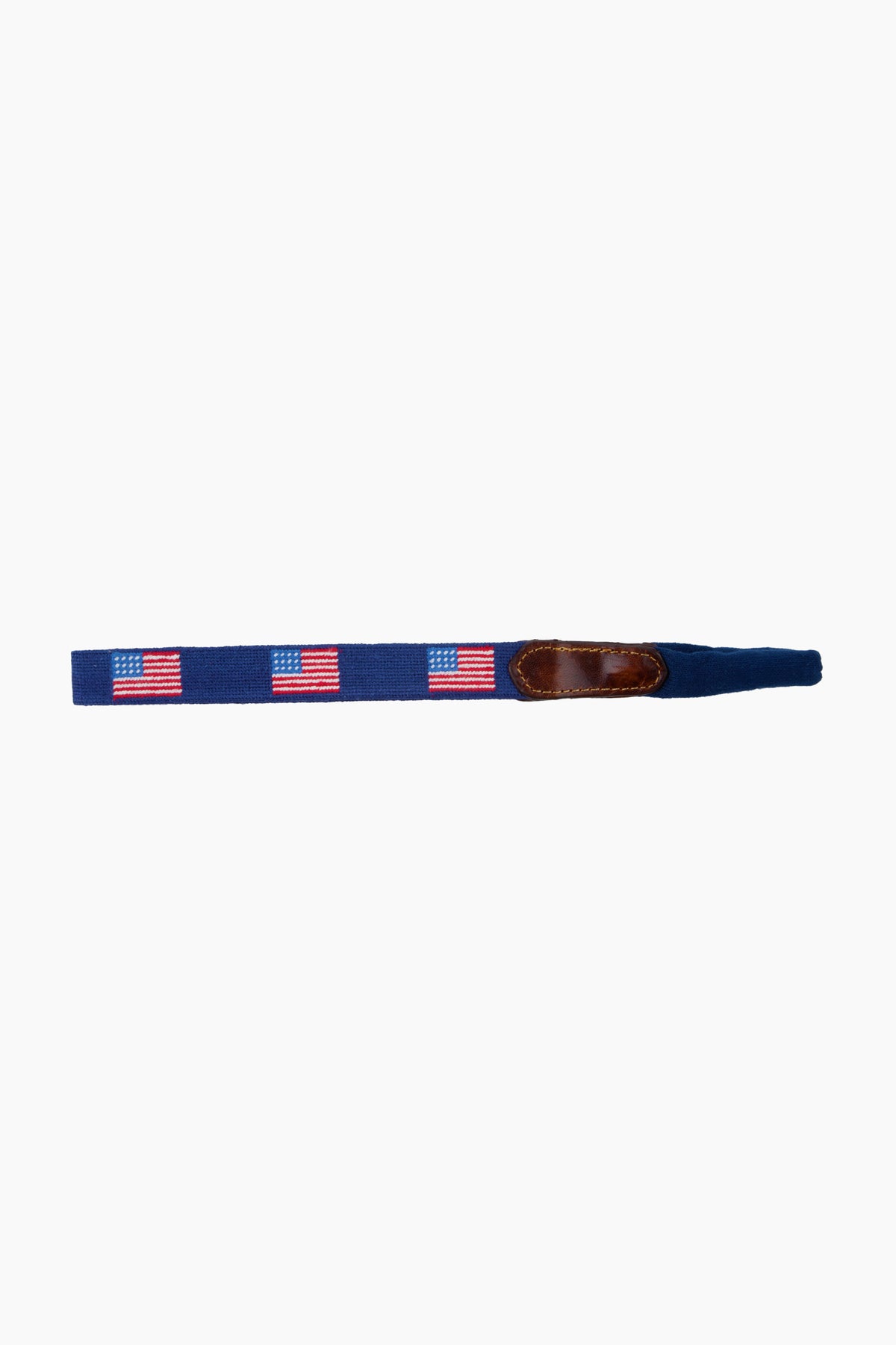 A navy blue fabric belt by Smathers and Branson, featuring hand-stitched American Flag needlepoint designs and a brown leather accent.