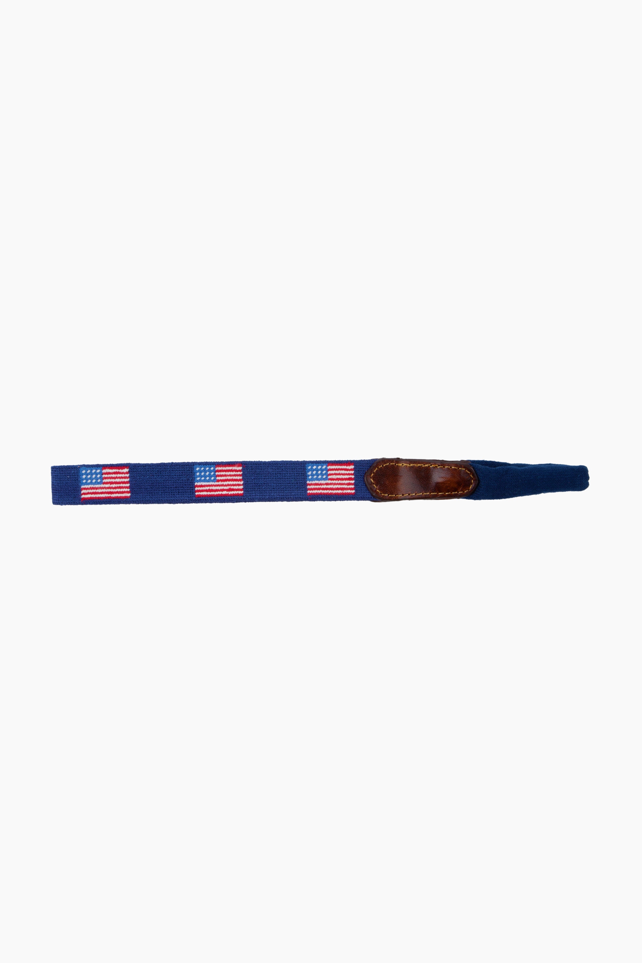 A navy blue fabric belt by Smathers and Branson, featuring hand-stitched American Flag needlepoint designs and a brown leather accent.