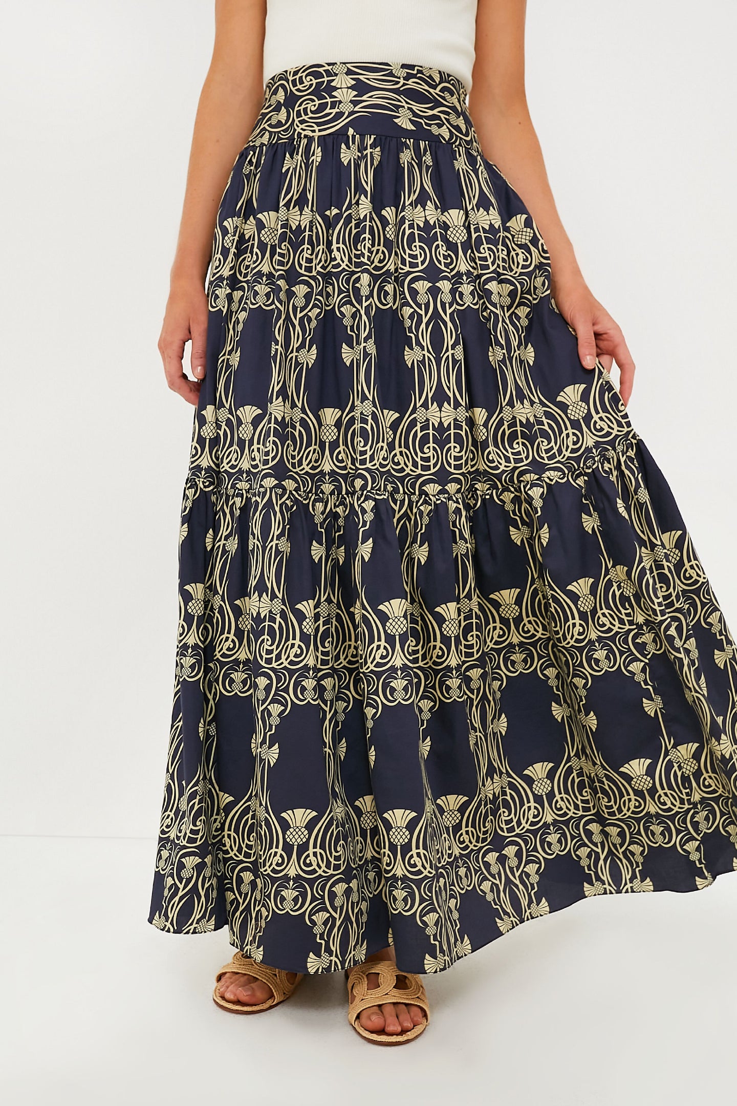 A person wears an Eugenia Fernandez navy blue and yellow patterned cotton maxi skirt with a white top and brown sandals—an effortless, sustainable fashion look.