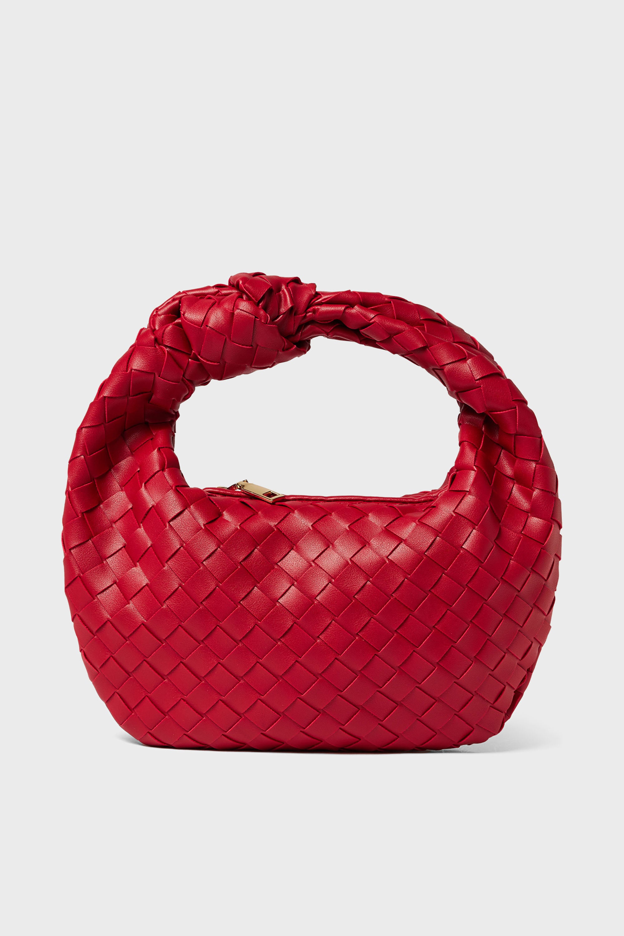 The Urban Expressions handbag is small, round, and made from woven vegan leather in red, featuring a knotted handle and zipper closure.