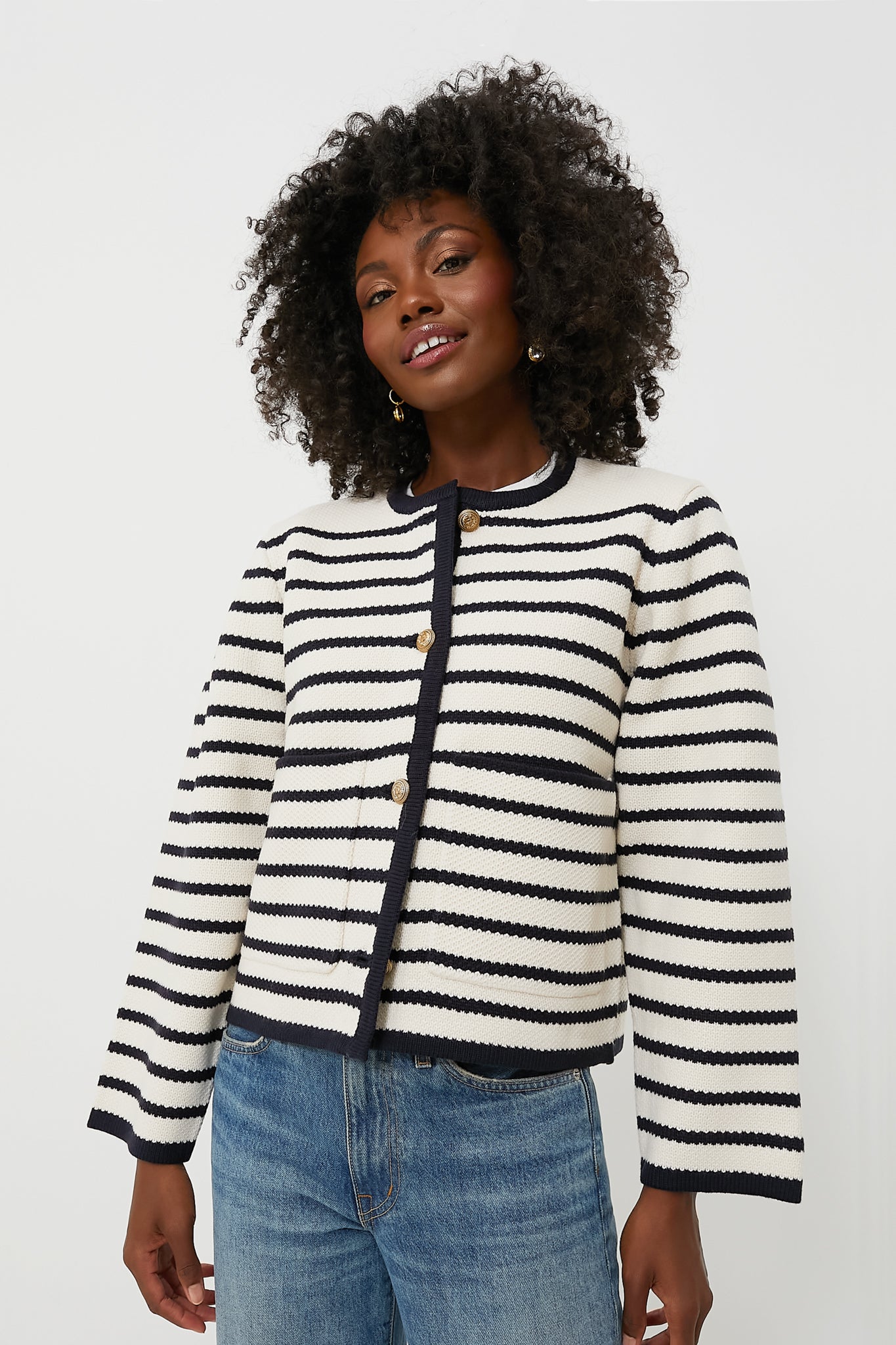 A person wears a Moon River white and black striped cardigan with gold buttons and blue jeans, featuring a cropped hem.