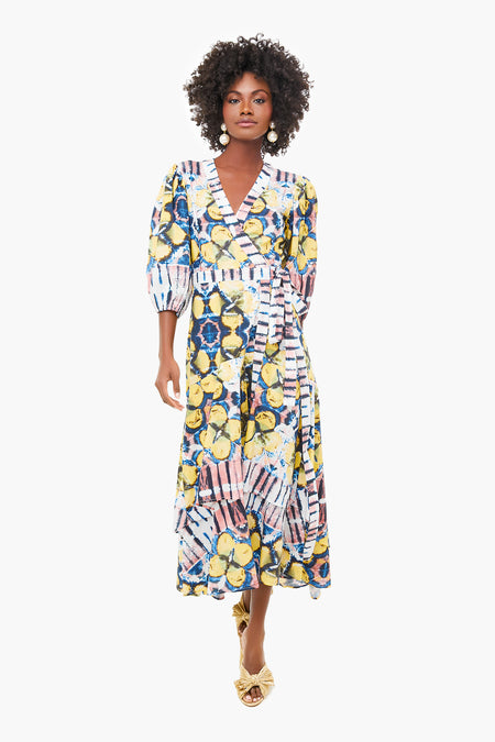 A woman wearing the ALEXIS Marsai Dress—a colorful, patterned piece with puffed sleeves, gold sandals, and an A-line midi skirt—makes this standout style a must-have in womenswear.